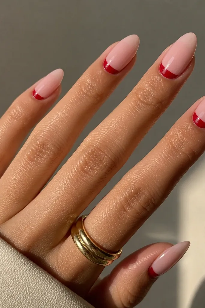 Almond nails that are mostly sheer blush-pink, with a clean red half-moon at the cuticle on each nail, the red shape is curved and crisp like a crescent.