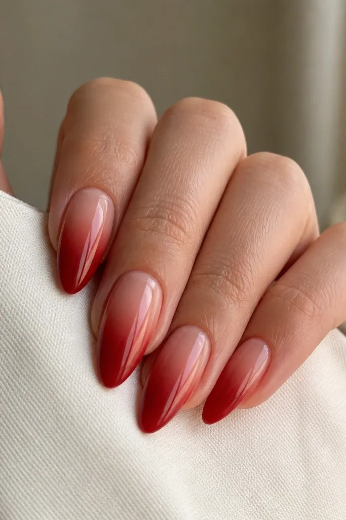 Almond nails with a smooth ombre gradient: deep red at the tip blending into a sheer nude base, the transition is soft and fades upward without harsh lines.