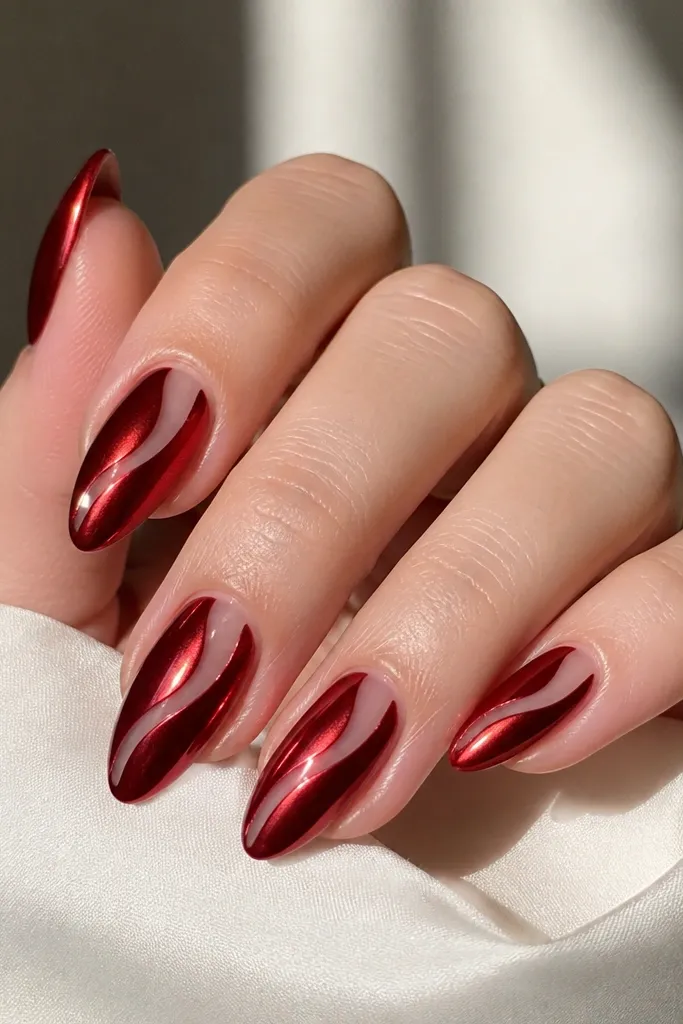 Almond nails with a red chrome finish, and a clear negative-space swirl that starts near the cuticle and curves toward the side, leaving a transparent glossy path through the chrome.