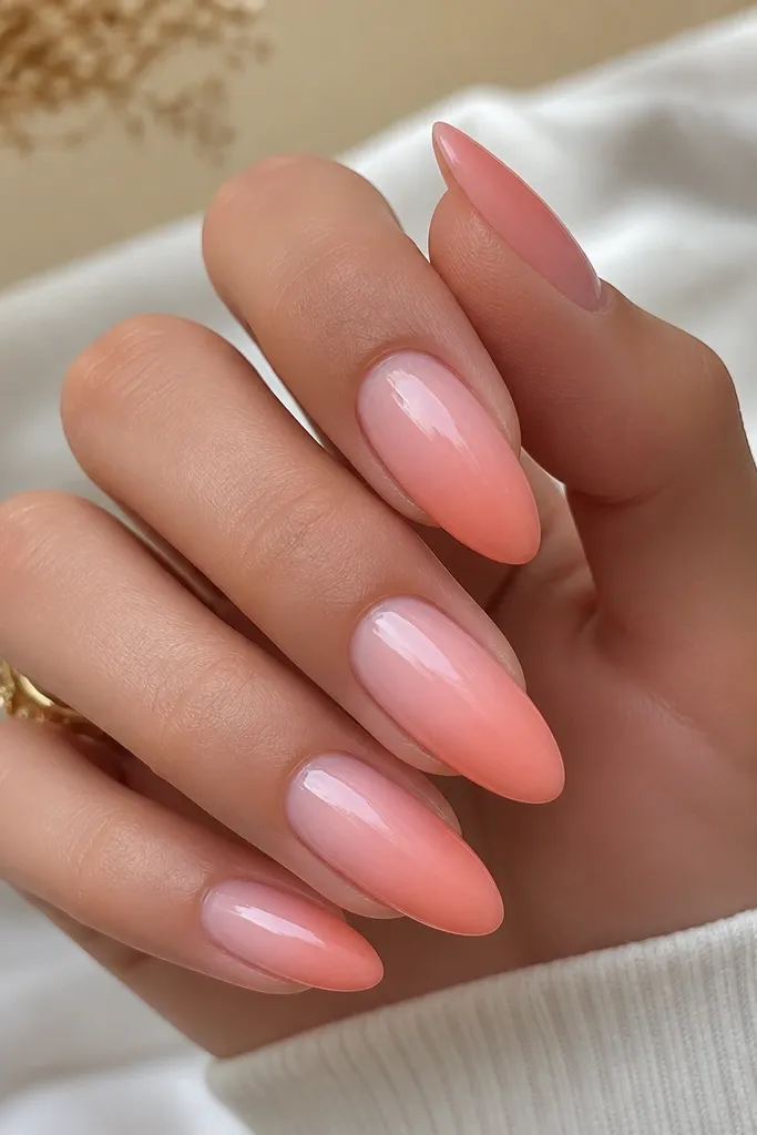 Glossy almond nails with an ombre that fades from warm baby pink near the cuticle into a slightly deeper peachy pink at the tip. The transition is smooth with no visible line.