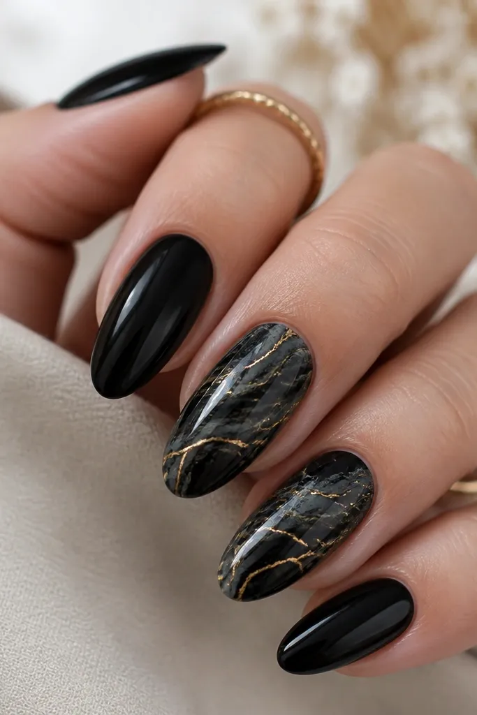 Two accent nails have black marble swirls with gray undertones and thin gold veining. The other nails are solid glossy black. Veins branch from the center toward the tips, glossy and fine.