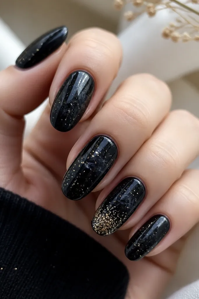 Glossy black nails with a galaxy effect. Small warm gold and champagne glitter dots are scattered like stars, with a few soft swirls in the background. One nail has a denser glitter cluster near the tip.