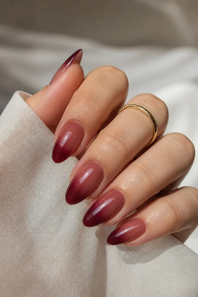Almond nails with a sheer warm wine tint on the base, with slightly deeper color concentrated toward the tip. The finish is glossy and looks like a tinted manicure rather than opaque paint.