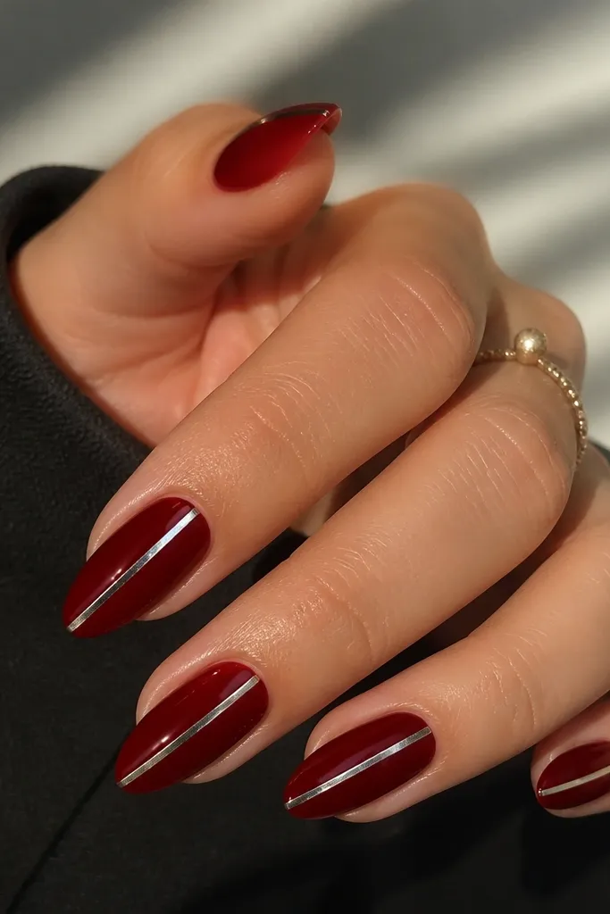 Almond nails in dark red with a single thin chrome strip running vertically from near the cuticle toward the tip on each nail. The strip is bright silver and glossy, contrasting with the deep red background.