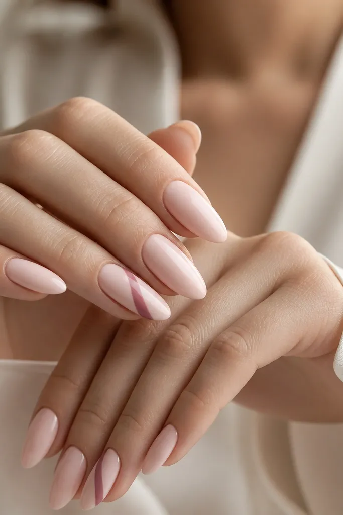 Almond nails with a soft blush base. On accent nails, a diagonal ribbon of slightly deeper pink runs from lower side near the cuticle to the upper tip, with a clean edge.