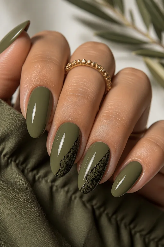 Almond nails painted smoked olive green with a glossy finish. On two accent nails, black lace-like stamping covers the outer third, with fine linework and crisp edges.