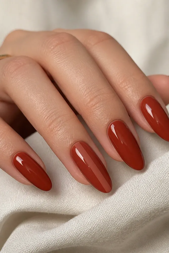 Almond nails painted glossy rusty red. On the middle finger, one vertical stripe is matte instead of glossy, running from near the cuticle to the tip. The stripe is clean and narrow.