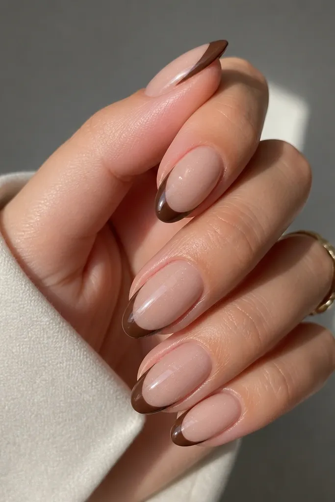 Short almond nails with a sheer nude base, espresso-brown French tips, and a fine micro-shimmer that glints along the tip edge; each nail has a glossy gel top coat with sharp, centered smile lines.