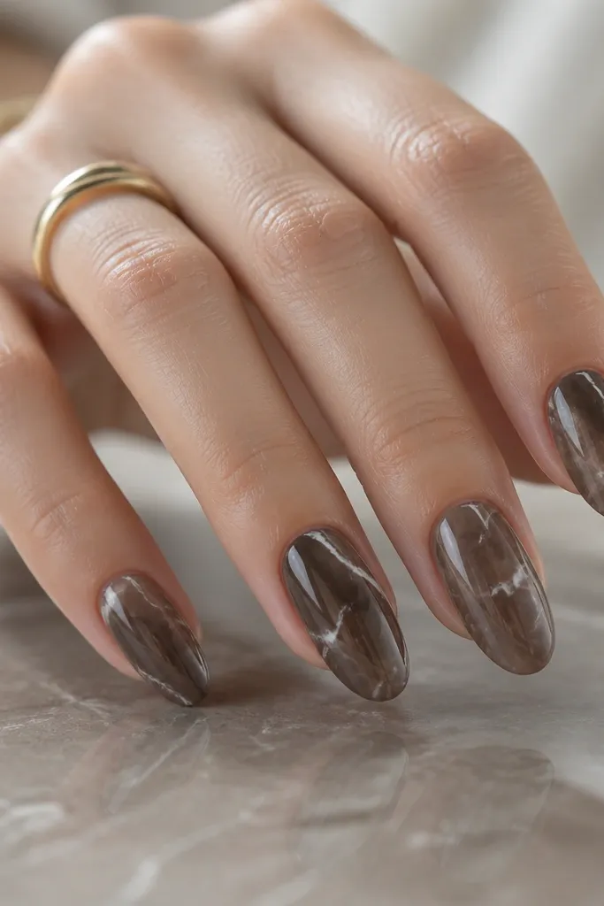 Mocha brown marble nails with thin white vein lines branching across the nail; glossy finish makes the marble look like polished stone.