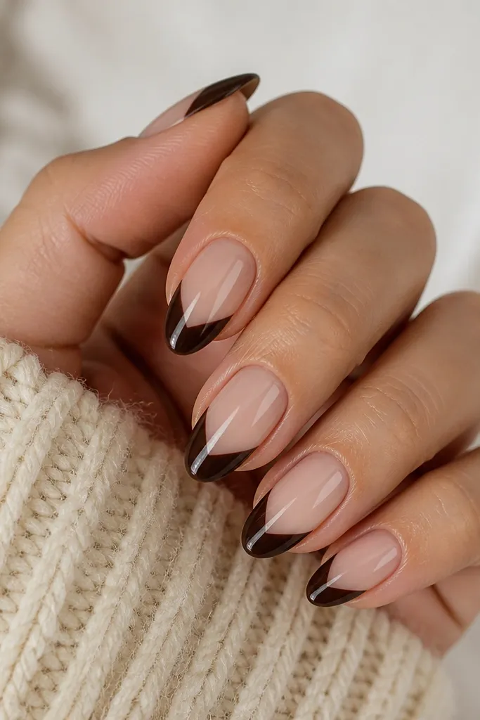 Short almond nails with a nude base. The tips are chocolate brown but shaped like almond caps with a clear negative-space V near the center. The negative space is crisp and glossy, creating a clean modern look.