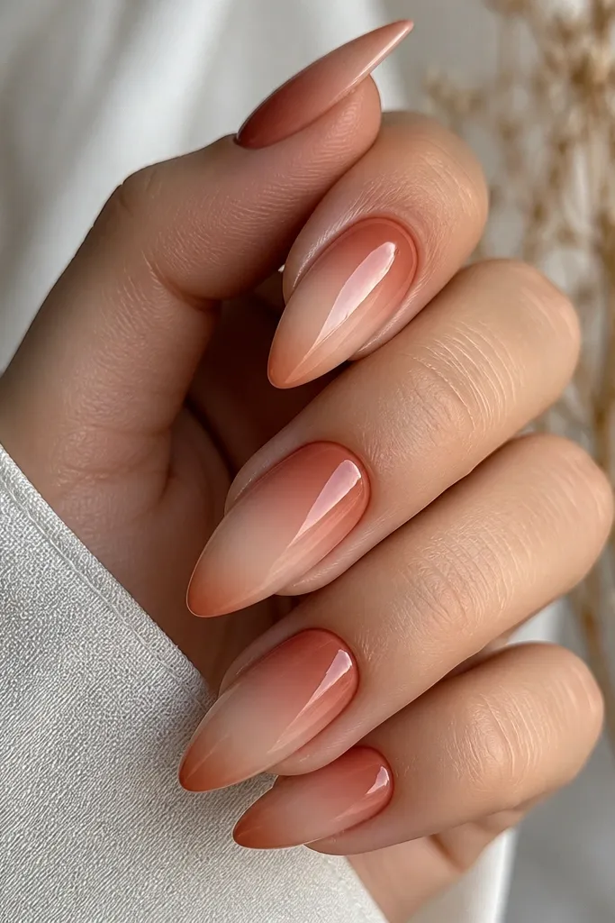 Long almond nails. The base is a reverse ombre: deeper terracotta at the cuticle fading to sheer nude toward the middle. The French tip is a soft terracotta fade that blends into the nude, with no hard line, and a glossy finish.