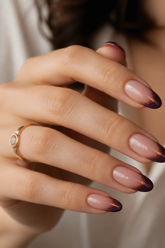 Medium almond nails. The base is sheer nude with glossy finish. French tips are smoke plum - deep purple with a slightly smoky center glow. On top of the tips, there's a fine copper chrome dust effect, concentrated near the center.