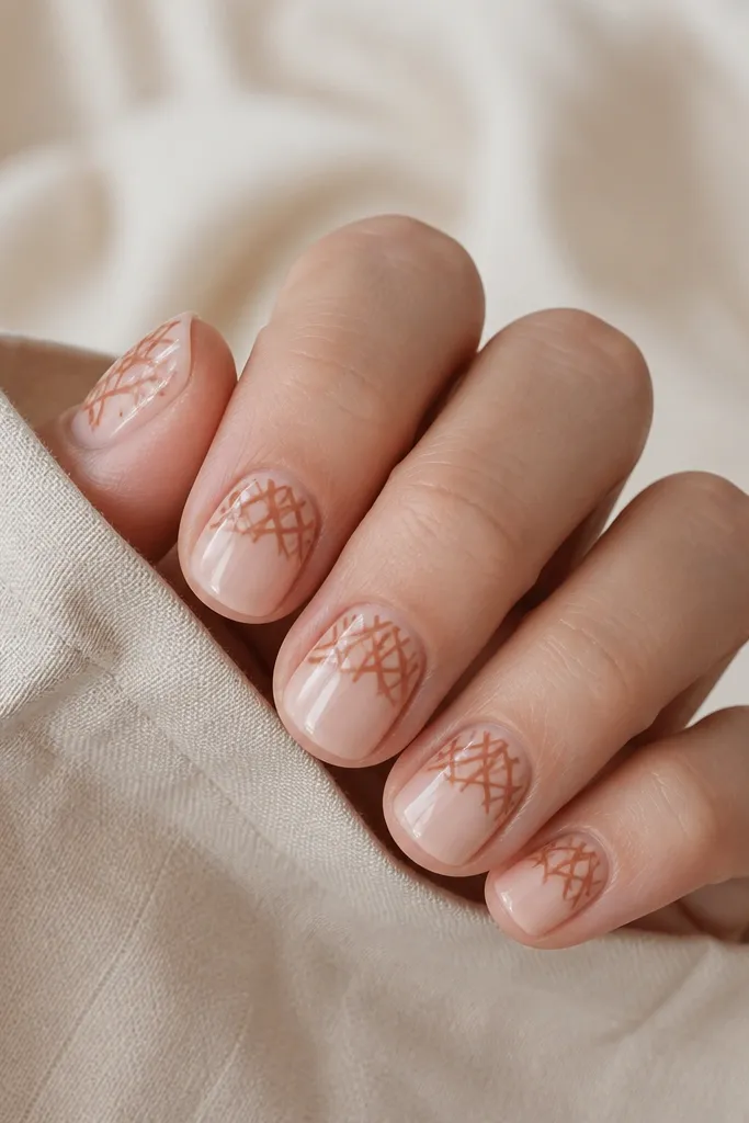 Short square nails with a sheer beige base. On each nail, there's a terracotta crisscross pattern that covers only the top half of the nail, like a half web. The lower half stays clear and glossy.