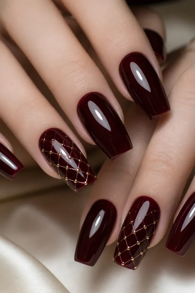 Glossy black cherry nails in a long squoval shape. On accent nails, rose-gold crisscross micro studs form a small grid pattern near the center and slightly toward the tip. The rest of the nails stay solid glossy cherry.
