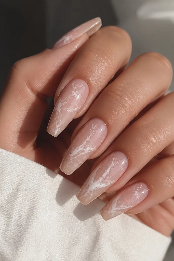 Coffin nails with a clear nude base that looks slightly translucent. Each nail has white marble swirls that look organic and veiny, concentrated toward the center and fading toward the edges. The finish is glossy and smooth, not gritty.