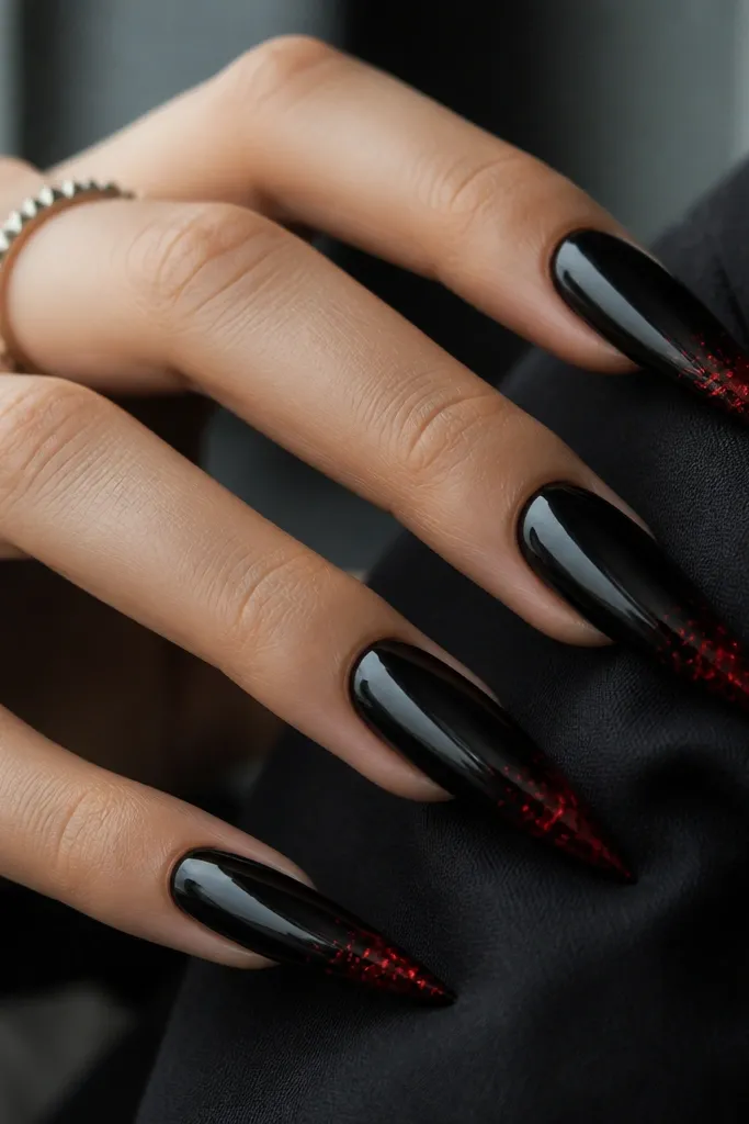 Stiletto-coffin nails painted glossy black. The tips have tiny red foil flecks concentrated at the very end, like a controlled burst, with sharp reflective shine.