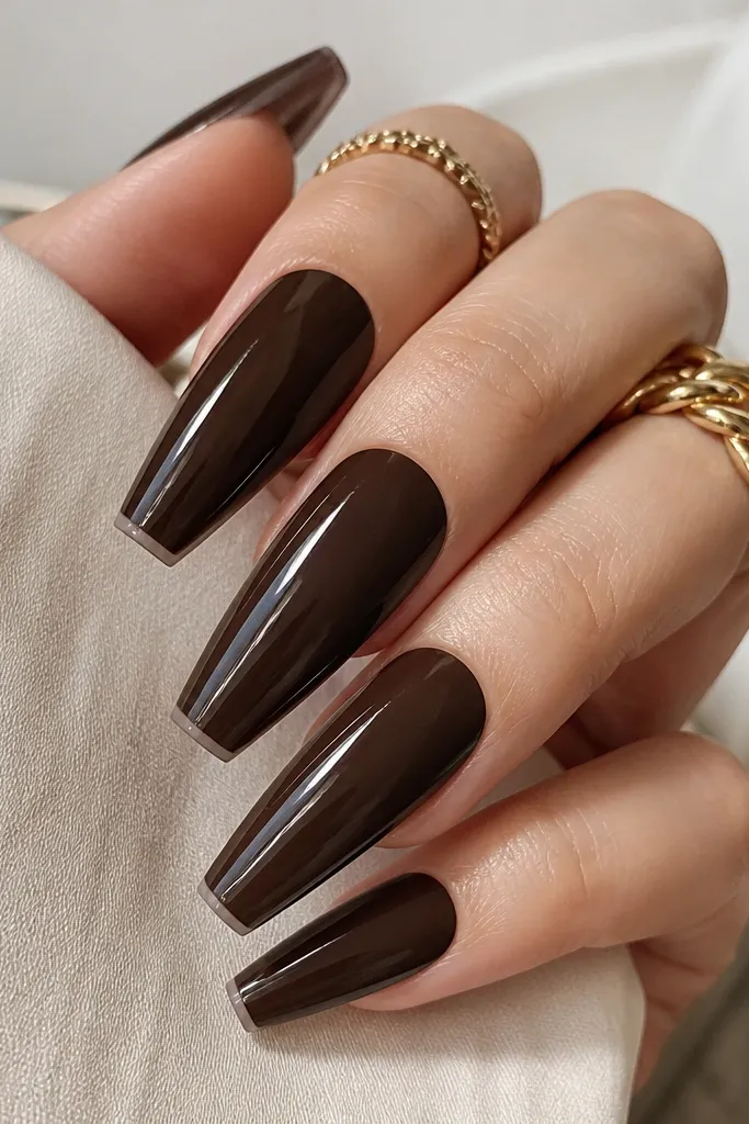 Coffin nails in deep chocolate brown glossy on top, with a subtle satin taupe showing along the underside near the tip edge. Light catches the glossy surface.