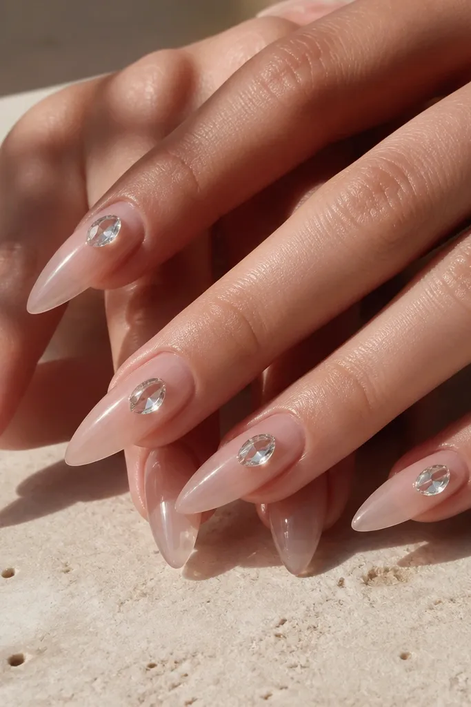 Long clear nude nails with a glossy finish. Each nail has a single 3D teardrop crystal placed slightly off-center near the cuticle or mid-nail.