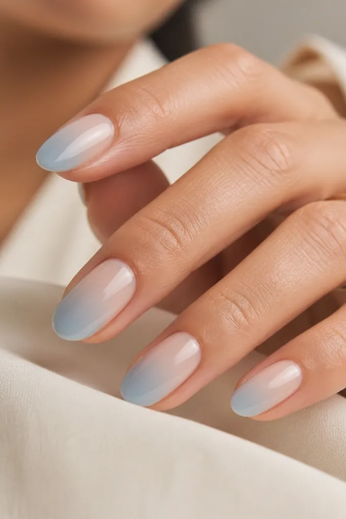 Nails painted in glossy nude. On each nail, a baby blue color fades from one side toward the center, like a soft gradient ribbon.