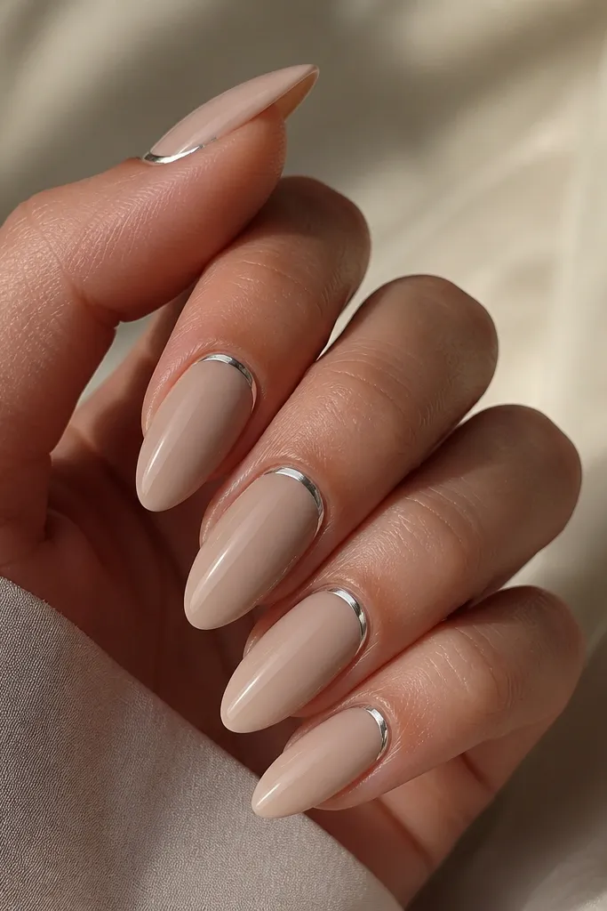 A set of long almond nails in a creamy nude base, with a thin chrome line running right along the cuticle and catching light like a silver visor.