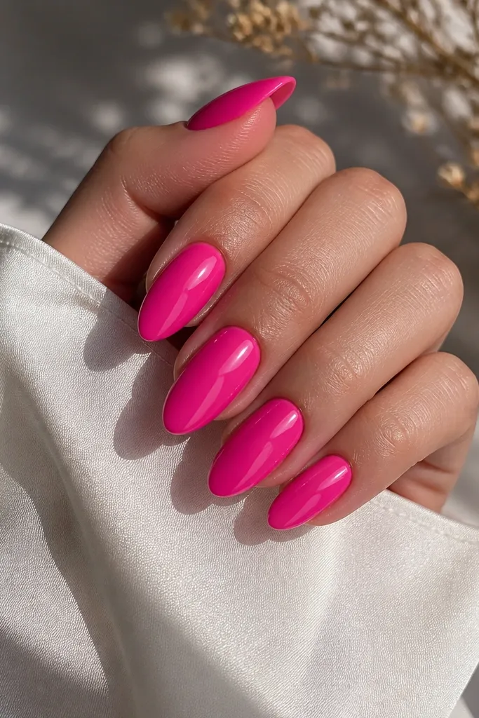 Long glossy almond nails in a vivid hot pink, with a mirror shine that reflects light like a candy wrapper.
