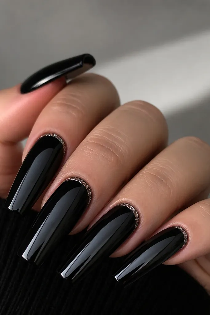 Long coffin nails painted in deep jet black with full mirror chrome. At the cuticle, a tiny crescent of silver micro-glitter sits in a narrow arc. The rest of the nail is pure dark mirror reflection with sharp edges.