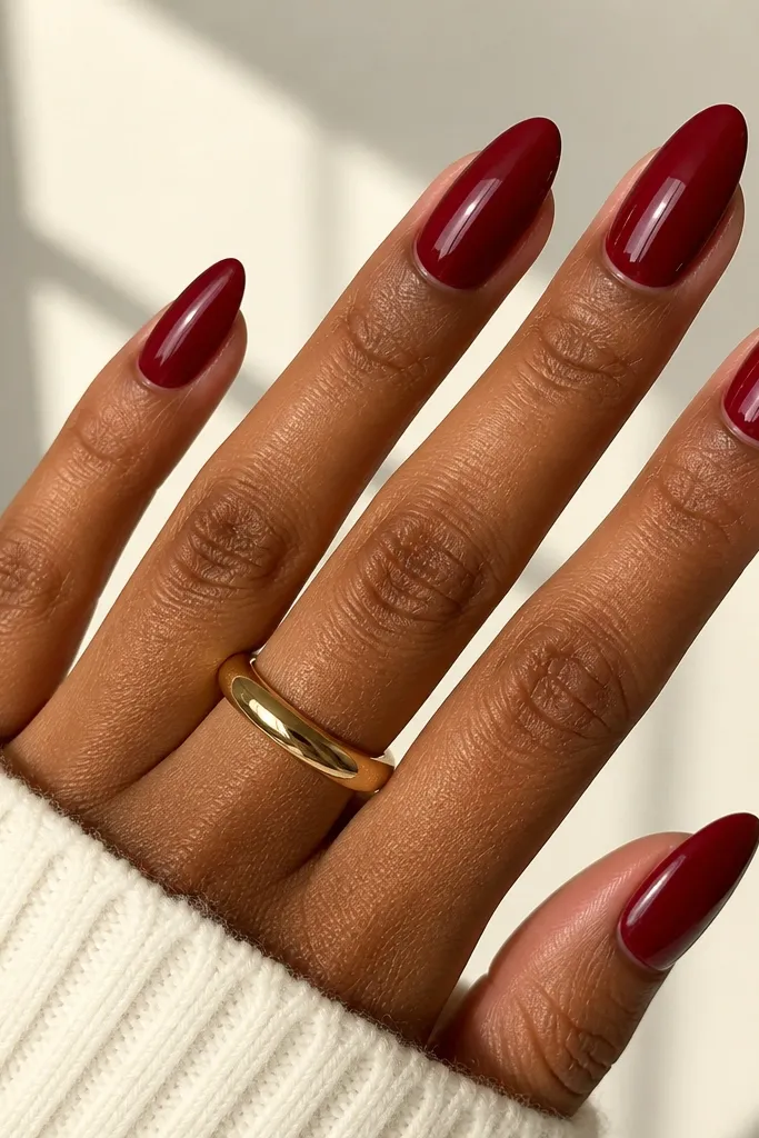Almond nails painted in a deep cherry red with a creamy, opaque finish. The gloss is high and the color looks solid, with no streaks or patchiness. Cuticles are clean and sharply defined.