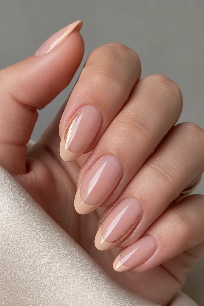 Medium almond nails with a sheer nude base and a nude-beige French tip. On one side of two accent nails, there's a small streak of copper foil under clear gel near the tip edge. Glossy top coat.