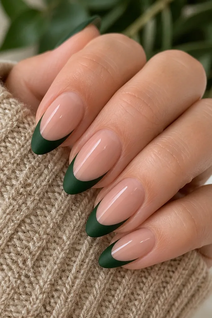 Medium almond nails with a sheer nude base. The French tips are deep evergreen green with a velvety matte finish. The nude base stays glossy, creating a two-texture contrast. No decorations.