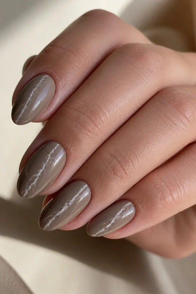 Short almond nails in an olive taupe nude. A thin white-gray marble vein runs straight down the center like a lightning bolt, with soft smoky edges. High shine top coat makes the marble look sealed under glass.