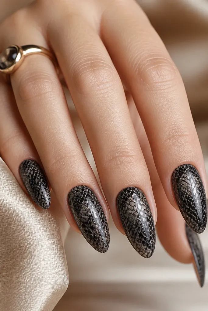 Almond nails with a black snake-skin pattern. The texture looks raised and scale-like, finished with a clear glossy topcoat that makes the scales look dimensional.