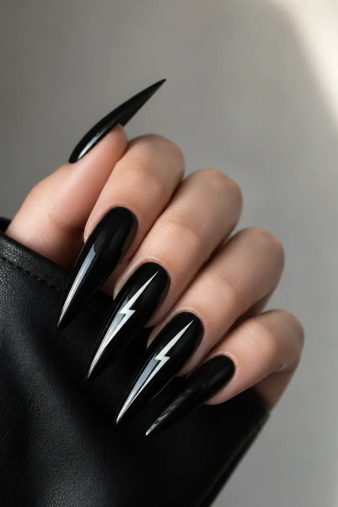 Very long stiletto nails painted glossy black. A thin white lightning bolt stripe runs diagonally across two accent nails. The stripe is sharp-edged and high contrast.