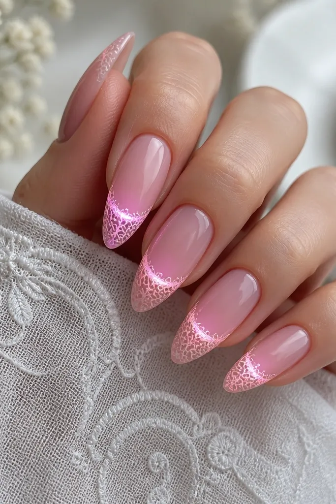 Long almond nails in soft pink. A lace-like white pattern is stamped near the tips, and a gentle LED glow sits under the lace area. The pattern looks fine and delicate, not chunky.