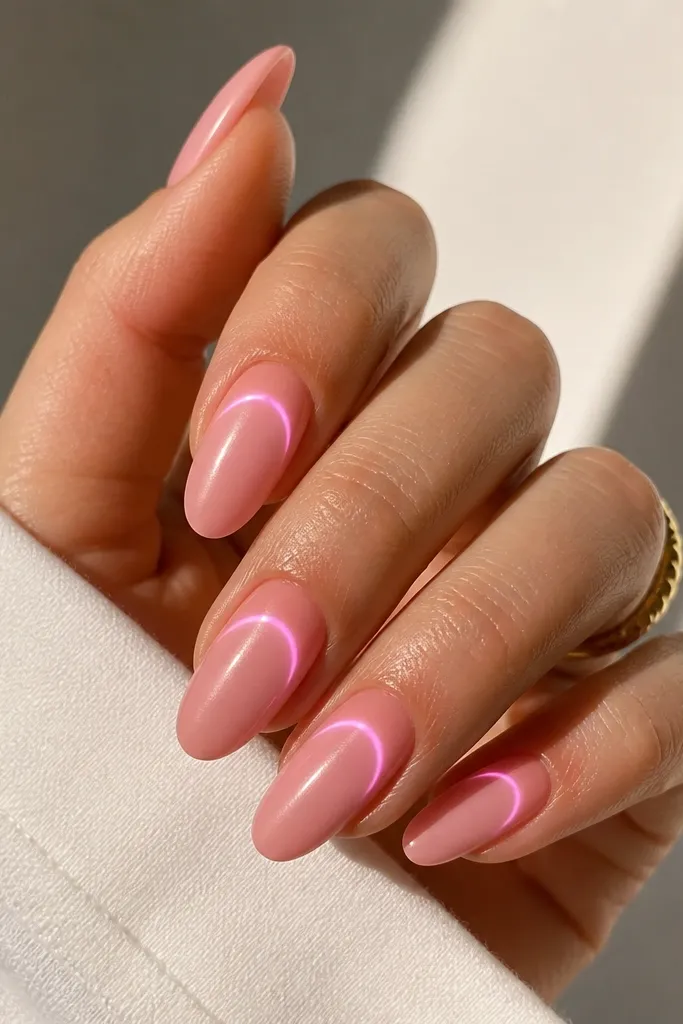 Almond nails with a satin-pink finish (not mirror). Under clear gel, a curved LED glow follows the nail's natural smile arc. The surface looks smooth like satin, with a controlled glow curve.