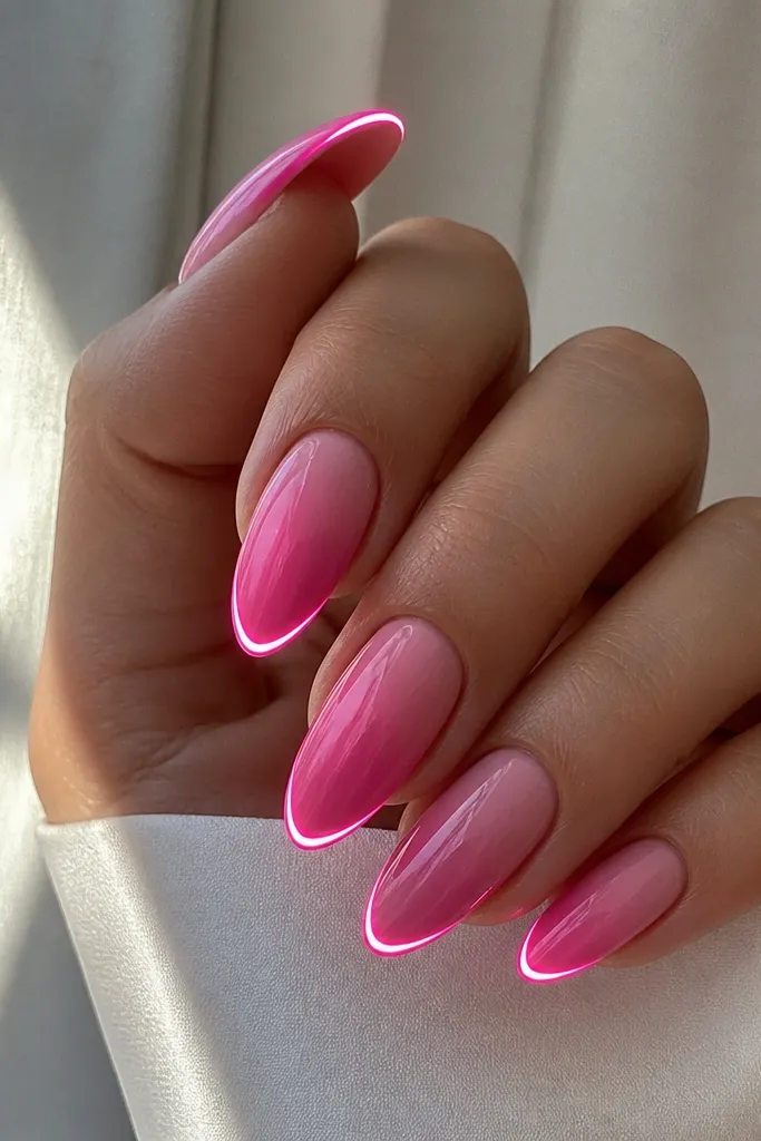 Almond nails with a Barbie-pink fade from deeper pink near the tip to lighter pink near the cuticle. A single bright LED strip runs along the tip edge, creating a spark-like glow line. The nails are glossy with a smooth finish.