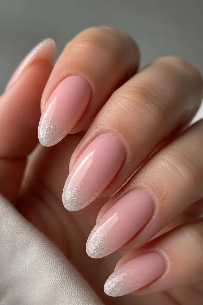 Glossy blush pink almond nails with a faint gradient of very fine silver micro-glitter only at the very tip, fading down; no glitter on the rest of the nail.