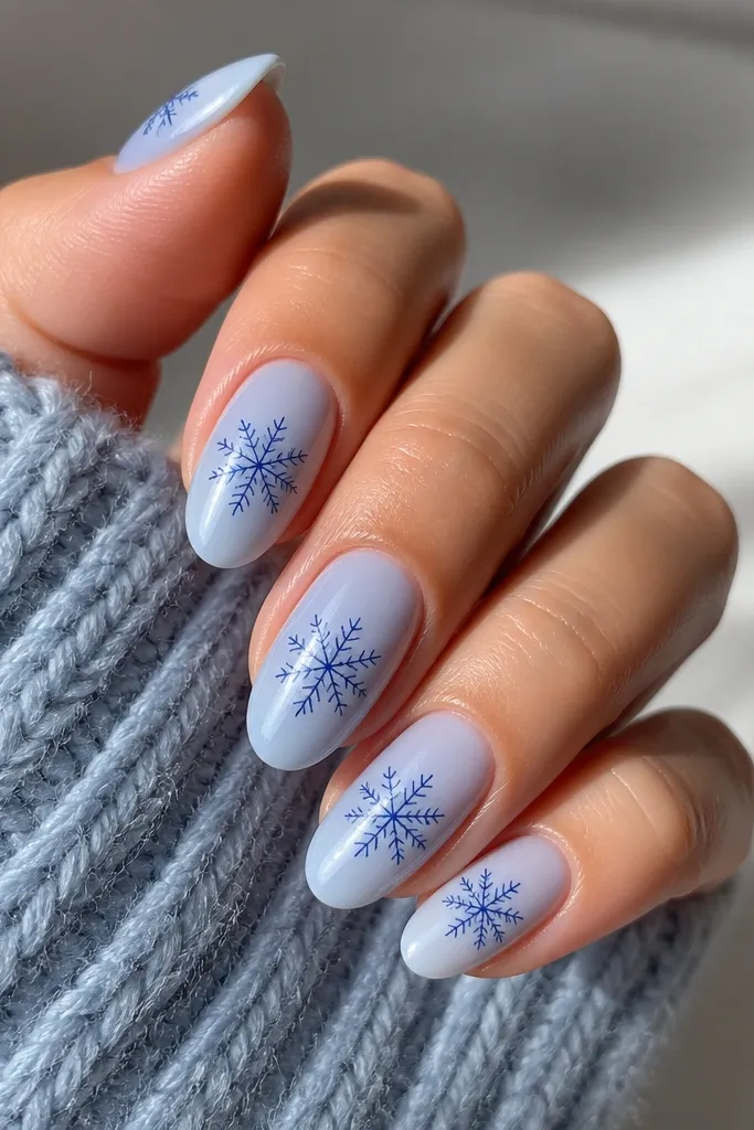 Medium almond nails with a sheer icy blue base. Each nail has one navy snowflake outline drawn near the center, with thin lines and no filled-in sections. The snowflake is slightly angled, with a clean negative space around it.