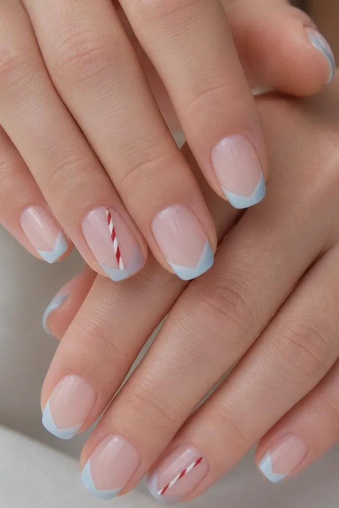 Short squoval nails with a sheer nude base. The tips are painted icy blue in a soft V shape. On two accent nails, a single candy-cane stripe runs diagonally from near the tip down to mid-nail in thin red-and-white lines.