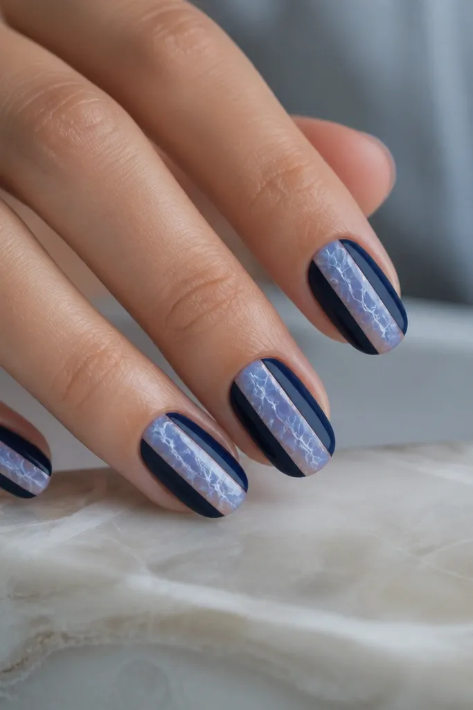 Nails with a navy base leaving two vertical negative-space panels in the center. Over the negative space, there is an icy blue marble veil with thin white veining like frost cracks.