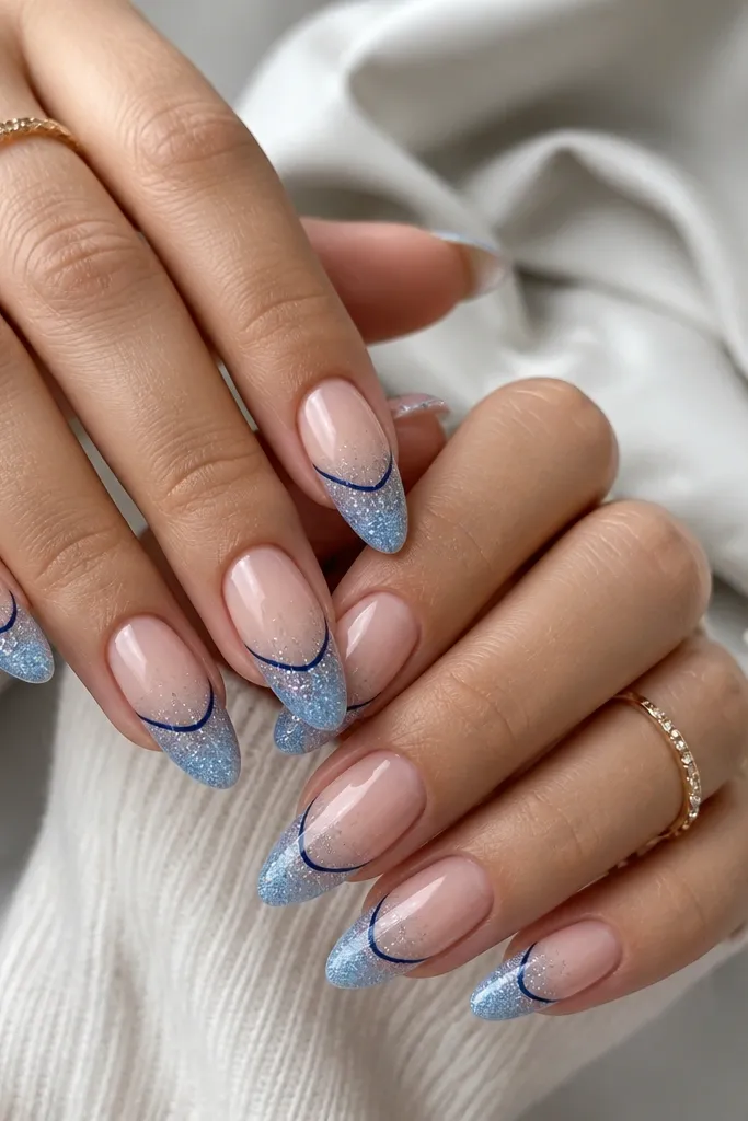 Almond nails with a sheer nude base. The lower half fades into icy-blue fine glitter, strongest near the tip and very light near mid-nail. A thin navy border line runs along the fade edge on each nail.