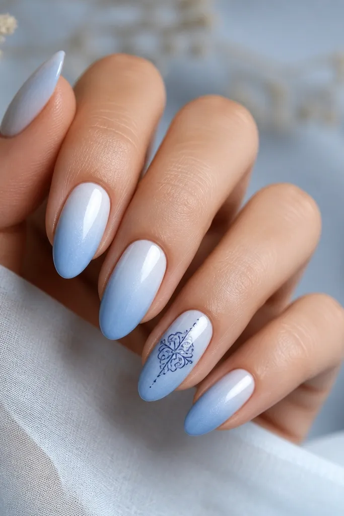 Medium almond nails with an icy blue gradient from lighter near the cuticle to slightly deeper blue toward the tip. One accent nail has a single thin navy ornament line drawing across the center. Other nails are plain gradient with no art.