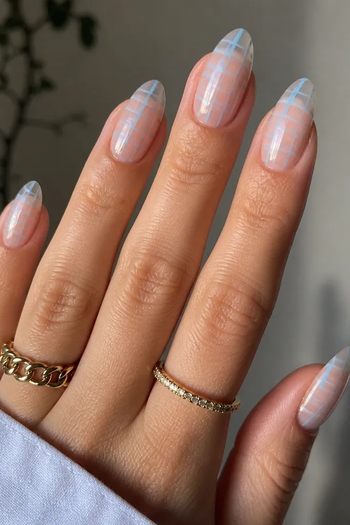Clear almond extensions with a sheer nude tint at the base. Over the center of each nail runs a micro check pattern in sky blue lines. The check is thin and evenly spaced, with a glossy top coat.