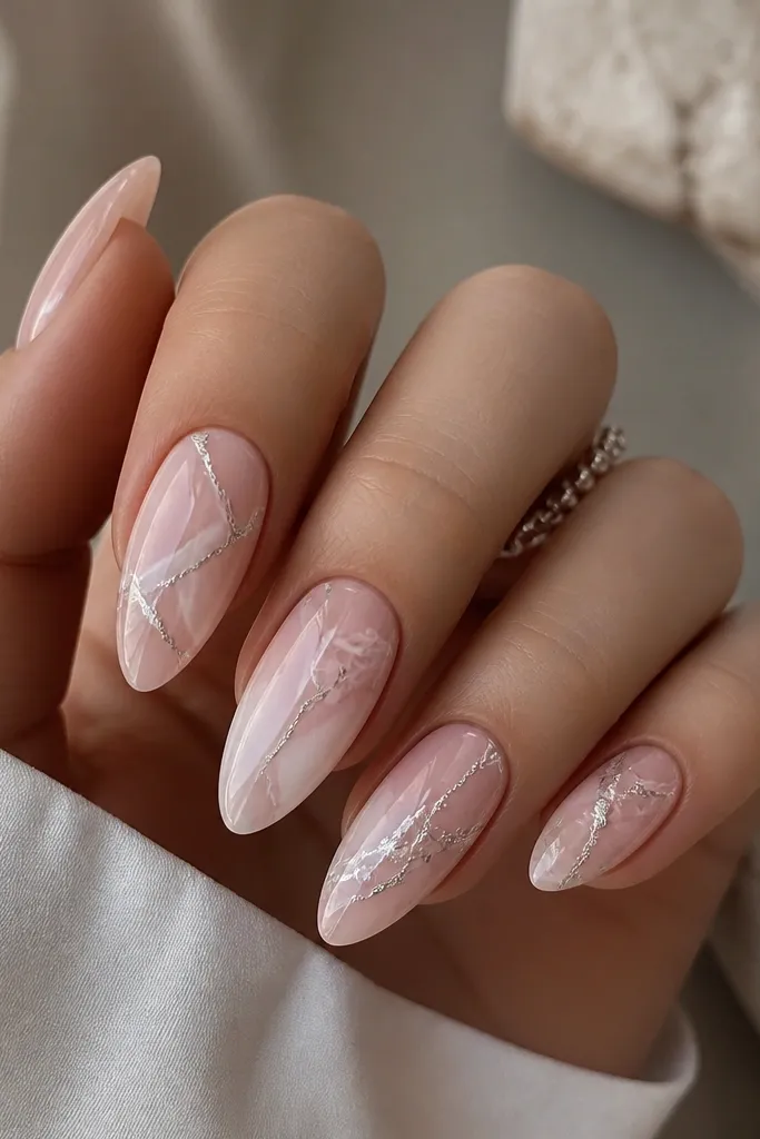 Soft pink almond nails with marble-style veining. Thin white-pink lines run through the nail, and silver chrome veins glow along the main streaks.