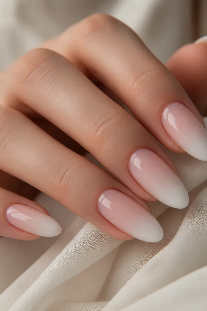 Almond nails with an ombré transition from sheer pink at the cuticle to milky white at the tip. The gradient is smooth, with no harsh line. The finish is glossy and the tip looks softly lit.