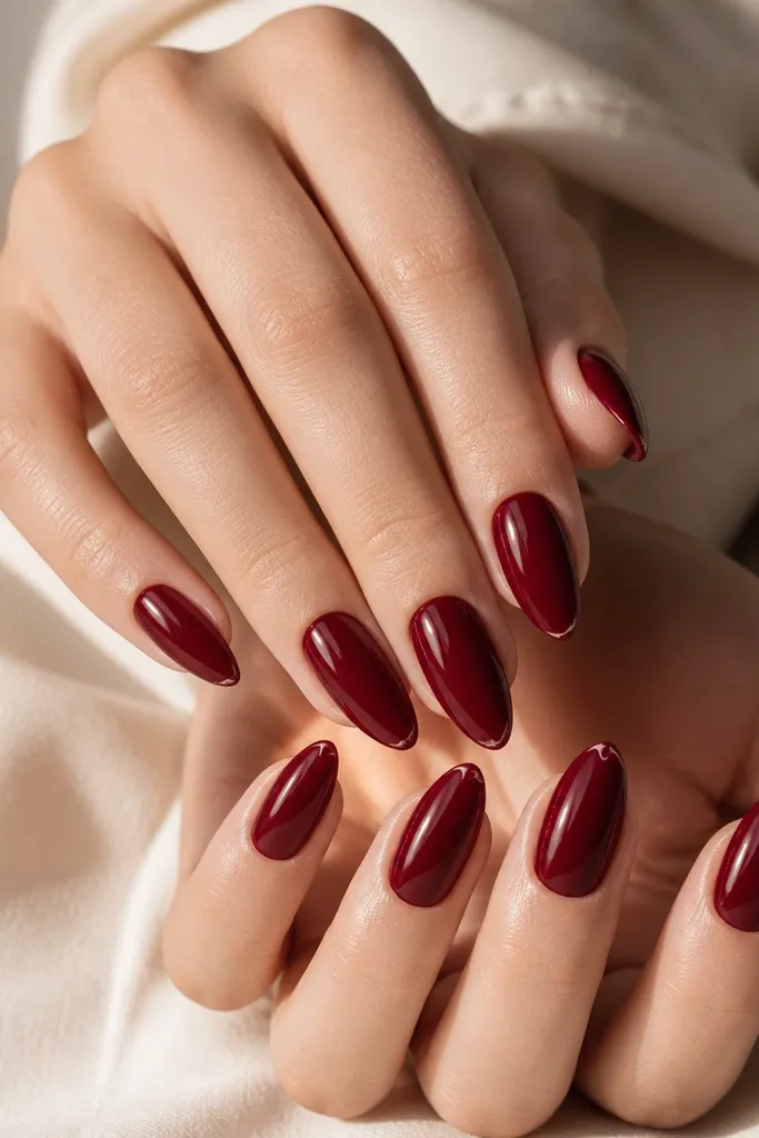 Ten almond nails painted a deep cherry red with a super glossy finish; each nail has a thin highlight line near the free edge that looks like a micro-gloss border.