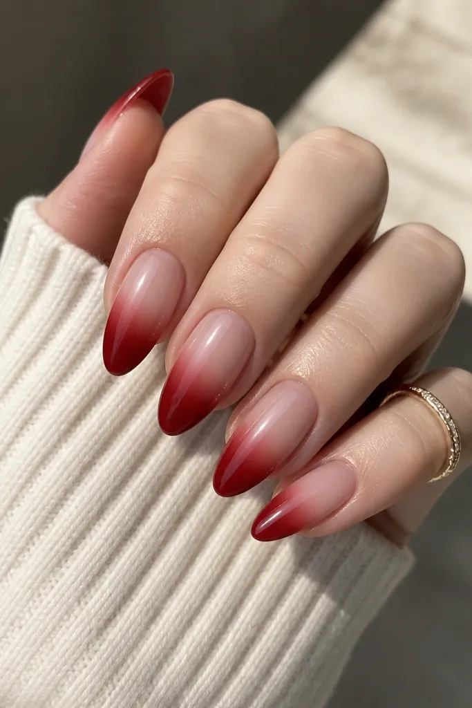 Almond nails with a gradient: deep red near the tip fading into a nude-pink base near the cuticle; the transition is smooth and glossy.