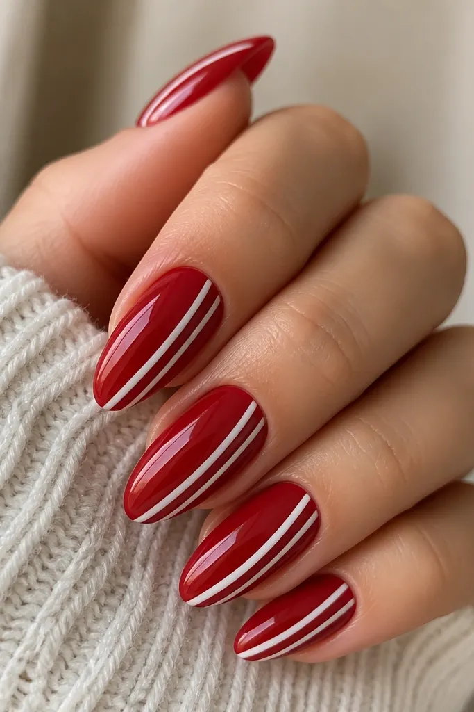 Almond nails painted glossy red with two thin white side stripes that run vertically from near the cuticle down the nail, slightly angled like candy cane lines.