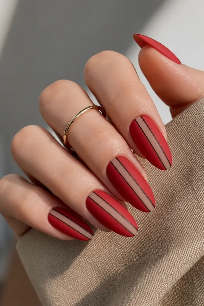 Almond nails in matte red with a vertical nude stripe; thin black micro lines outline the red blocks like graphic liner.