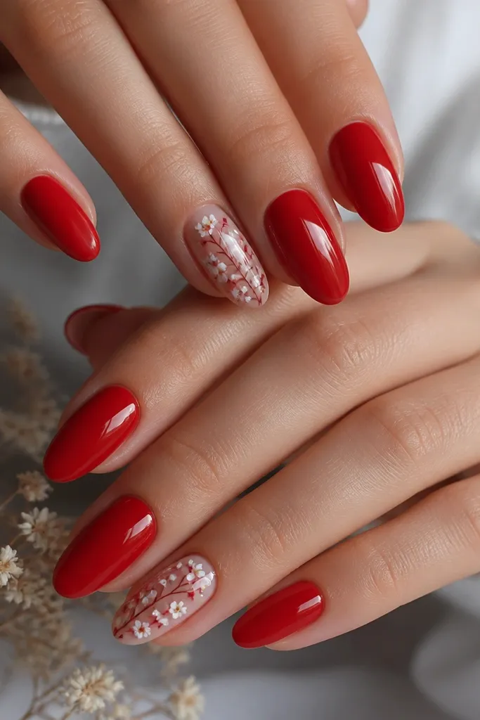 Most nails are glossy red almond; one or two accent nails have a delicate white and pale pink tiny floral pattern near the center with fine red stems, all under glassy top coat.