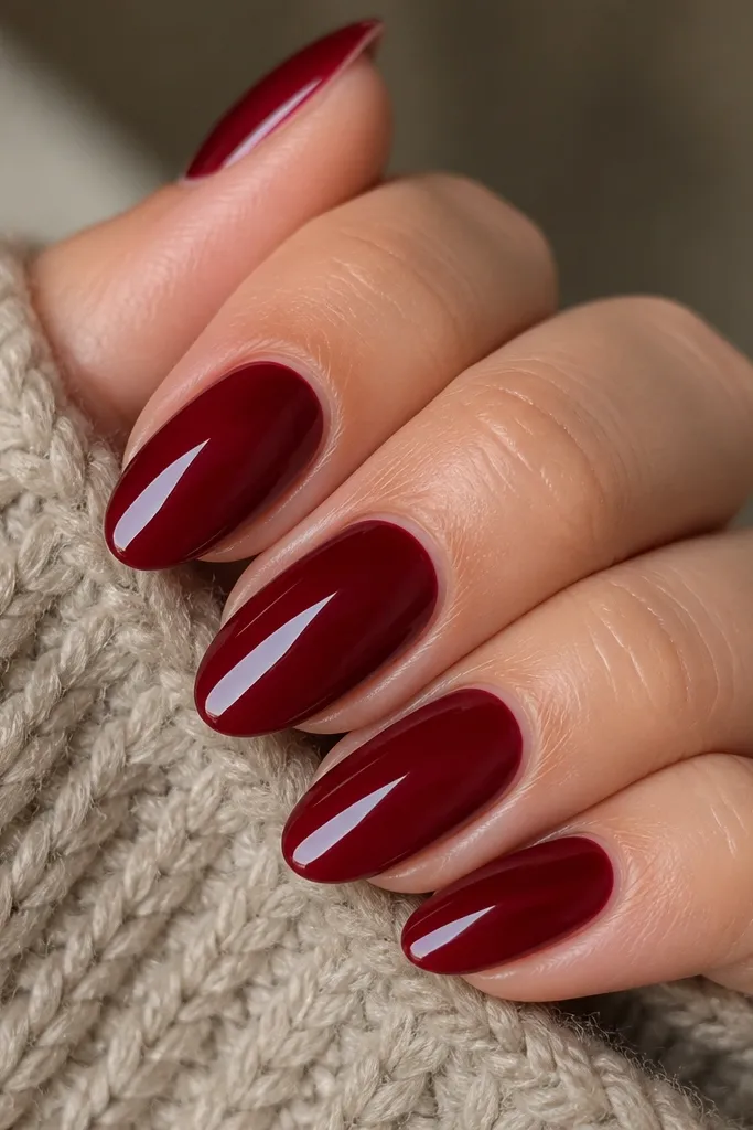 Close-up of short-to-medium red almond nails with a deep cherry red, mirror-gloss finish, smooth cuticle area, and a softly tapered tip. No nail art except a clean shine and crisp edges.